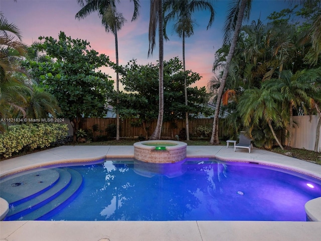 pool at dusk featuring an in ground hot tub