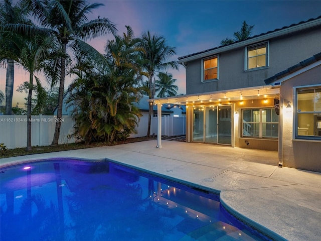 pool at dusk with a patio and a pergola