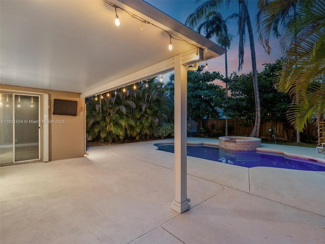 pool at dusk featuring a patio and an in ground hot tub