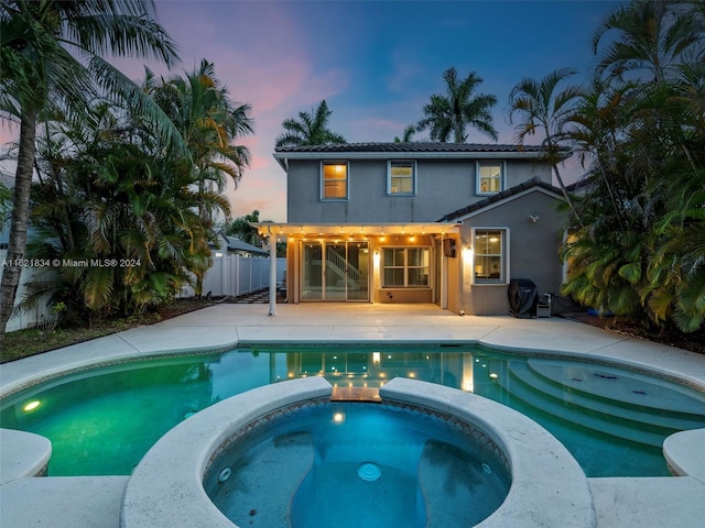 pool at dusk featuring a patio, a grill, and an in ground hot tub