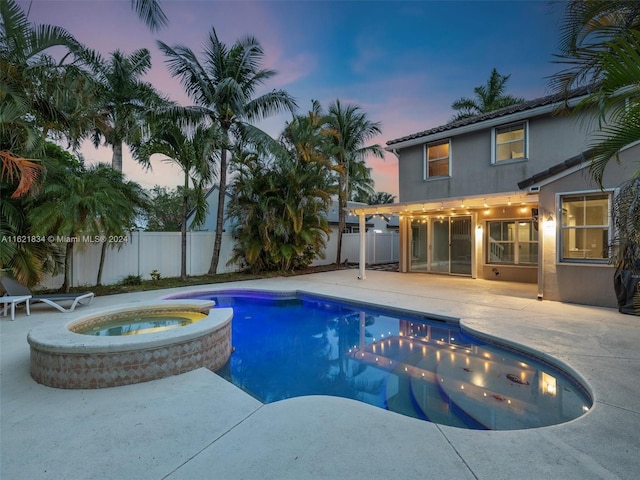 pool at dusk featuring a patio area and an in ground hot tub