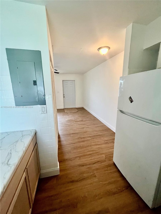 interior space with white fridge, electric panel, hardwood / wood-style floors, and tile walls