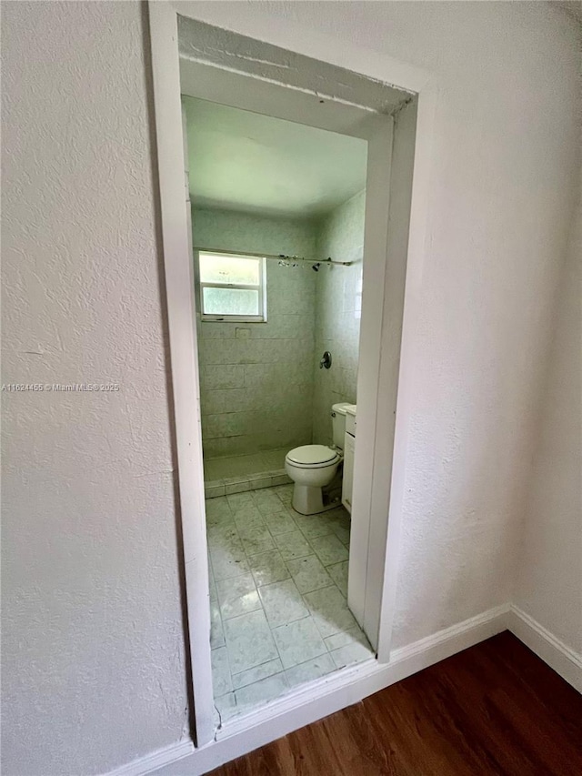 bathroom with a tile shower, hardwood / wood-style floors, and toilet