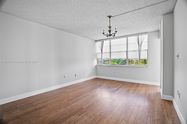 empty room with hardwood / wood-style floors, a textured ceiling, and a notable chandelier