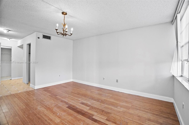 unfurnished room featuring light wood-type flooring, a textured ceiling, and a chandelier