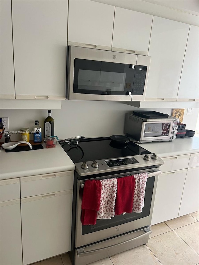 kitchen with appliances with stainless steel finishes, white cabinets, and light tile patterned floors