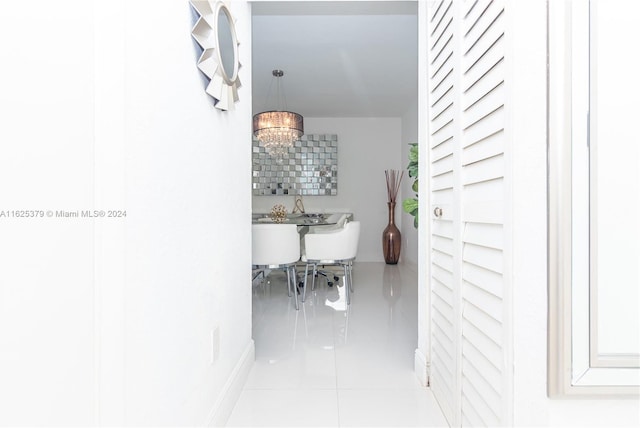 hallway with light tile patterned flooring and a notable chandelier