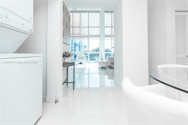 corridor featuring light tile patterned flooring, a wall of windows, and stacked washing maching and dryer