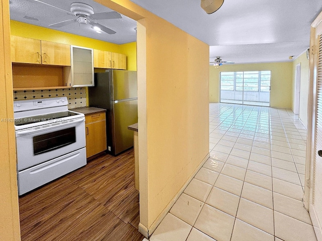 kitchen featuring light tile patterned floors, a ceiling fan, open floor plan, freestanding refrigerator, and white range with electric stovetop