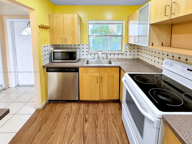 kitchen with light brown cabinets, stainless steel appliances, a sink, backsplash, and light wood finished floors