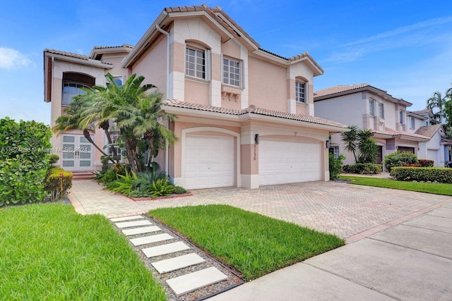 mediterranean / spanish home with stucco siding, an attached garage, a tile roof, and decorative driveway