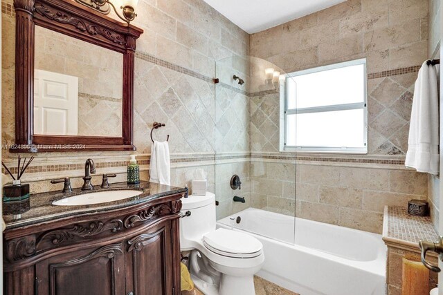 full bathroom featuring tile walls, tiled shower / bath, decorative backsplash, toilet, and vanity