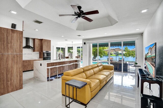 living room featuring light tile patterned flooring, a textured ceiling, ceiling fan, and a raised ceiling