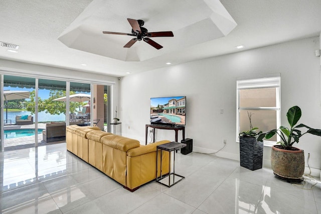 living room featuring ceiling fan, a textured ceiling, a tray ceiling, and light tile patterned floors