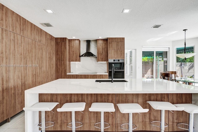 kitchen featuring light tile patterned floors, a textured ceiling, wall chimney exhaust hood, a kitchen breakfast bar, and sink