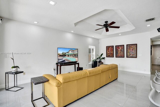 tiled living room featuring a textured ceiling, ceiling fan, and a tray ceiling