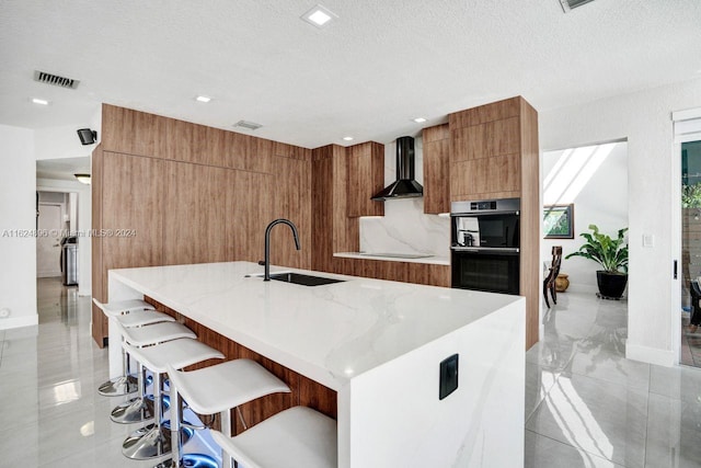 kitchen with a breakfast bar area, wall chimney range hood, sink, light tile patterned floors, and a spacious island