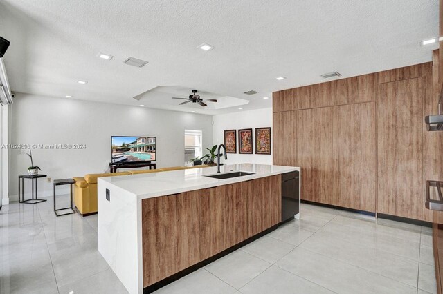 kitchen with light tile patterned flooring, ceiling fan, an island with sink, sink, and a textured ceiling