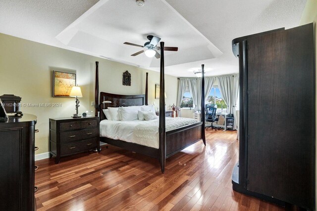 bedroom featuring ceiling fan, a textured ceiling, hardwood / wood-style floors, and a tray ceiling