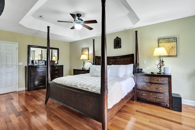 bedroom with ceiling fan, light wood-type flooring, and a tray ceiling