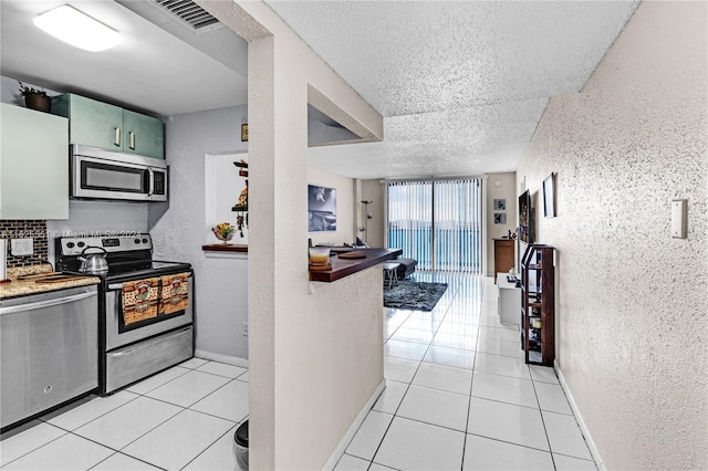 kitchen featuring light tile patterned floors, a textured ceiling, green cabinets, appliances with stainless steel finishes, and decorative backsplash