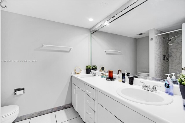 bathroom featuring tiled shower, toilet, tile patterned floors, and dual bowl vanity