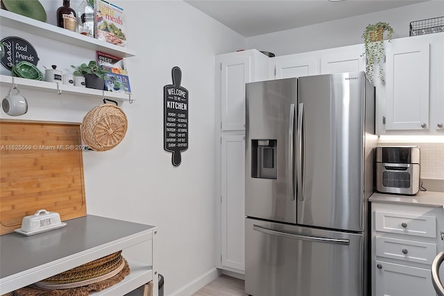 kitchen featuring stainless steel refrigerator with ice dispenser, white cabinetry, and backsplash