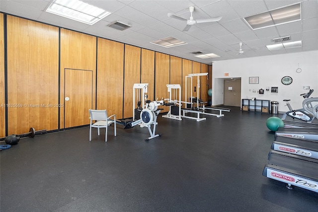 workout area with a paneled ceiling, wooden walls, and ceiling fan