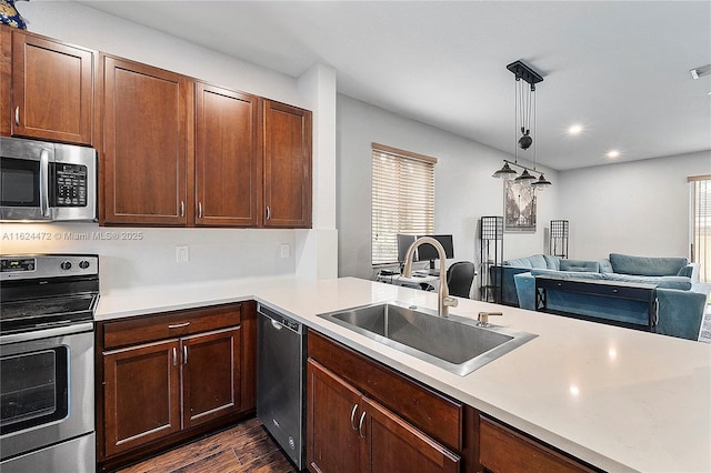 kitchen with stainless steel appliances, decorative light fixtures, sink, dark hardwood / wood-style floors, and kitchen peninsula