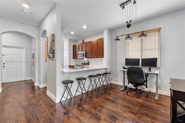 kitchen with kitchen peninsula, hanging light fixtures, appliances with stainless steel finishes, a kitchen bar, and dark hardwood / wood-style floors