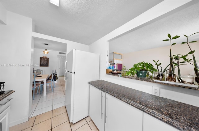 kitchen featuring light tile patterned flooring, white cabinetry, a textured ceiling, dark stone counters, and white refrigerator