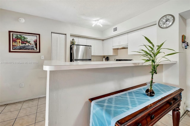 kitchen featuring white cabinets, kitchen peninsula, stainless steel refrigerator, a textured ceiling, and light tile patterned flooring