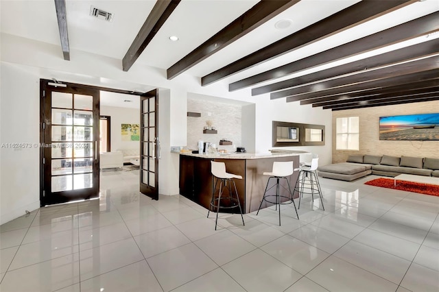 interior space with beamed ceiling, a breakfast bar area, french doors, light stone countertops, and light tile patterned flooring