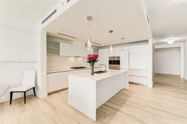 kitchen with white cabinets, decorative light fixtures, double oven, an island with sink, and sink