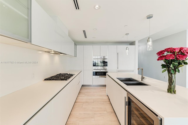 kitchen featuring beverage cooler, white cabinets, appliances with stainless steel finishes, decorative light fixtures, and sink