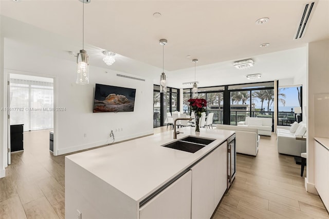 kitchen with decorative light fixtures, sink, white cabinetry, and a center island with sink