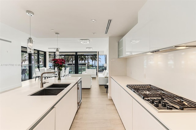 kitchen with white cabinetry, plenty of natural light, stainless steel gas cooktop, hanging light fixtures, and sink