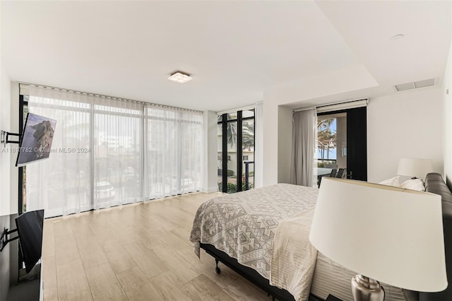 bedroom featuring expansive windows, light hardwood / wood-style flooring, and access to outside