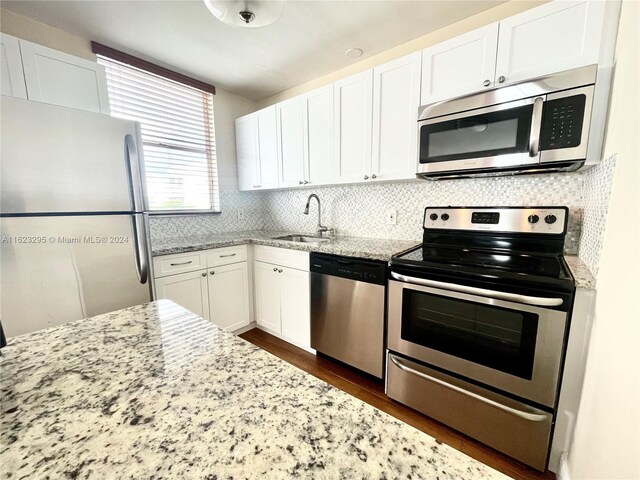 kitchen featuring white cabinets, light stone countertops, appliances with stainless steel finishes, backsplash, and dark wood-type flooring