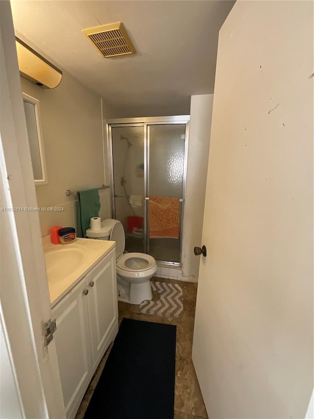 bathroom featuring a shower with shower door, vanity, toilet, and tile patterned floors