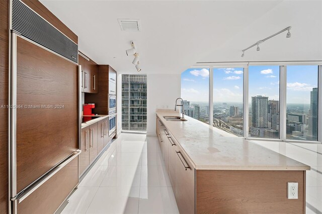 kitchen with light tile patterned floors, paneled refrigerator, light stone counters, track lighting, and sink