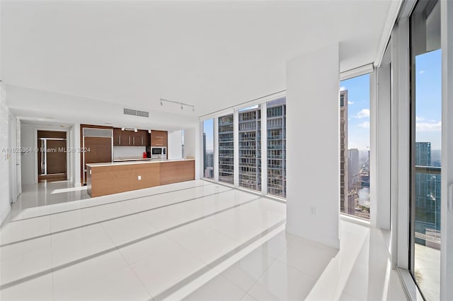 kitchen featuring light tile patterned floors, rail lighting, floor to ceiling windows, stainless steel microwave, and kitchen peninsula