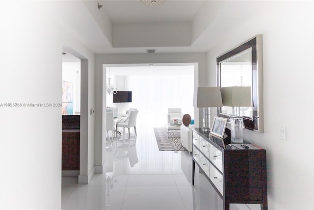 corridor with light tile patterned flooring and a tray ceiling