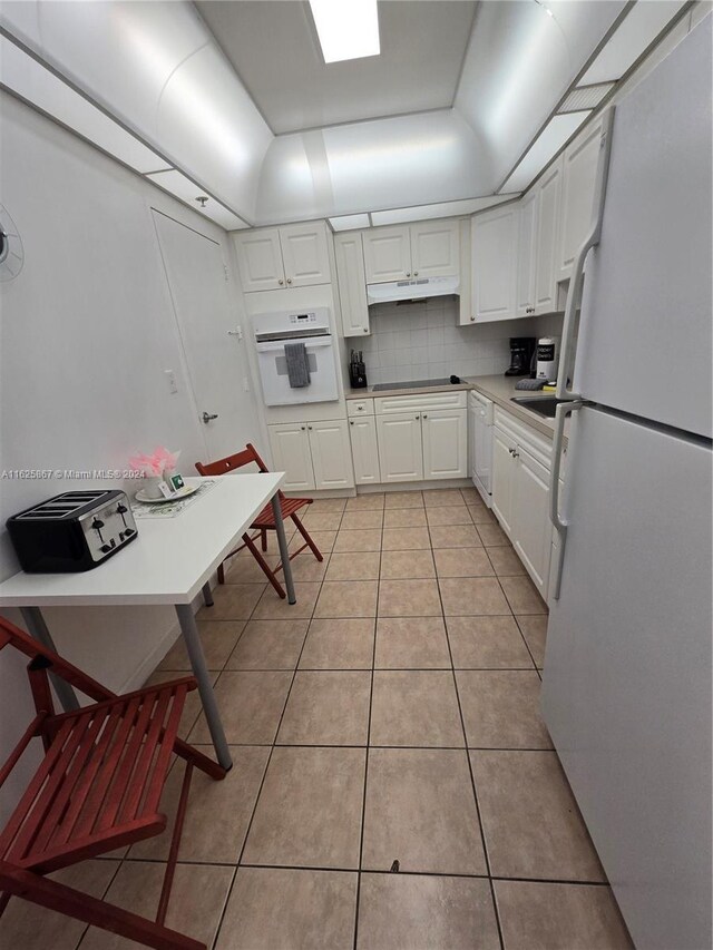 kitchen with light tile patterned flooring, tasteful backsplash, white appliances, and white cabinets