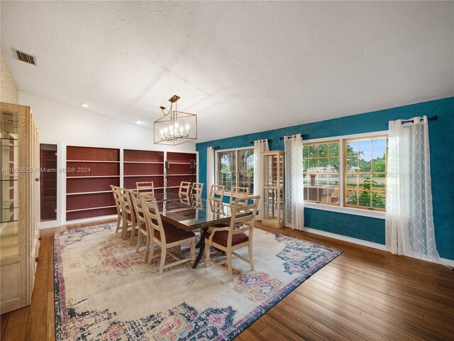 unfurnished dining area featuring a notable chandelier, a textured ceiling, hardwood / wood-style flooring, and vaulted ceiling