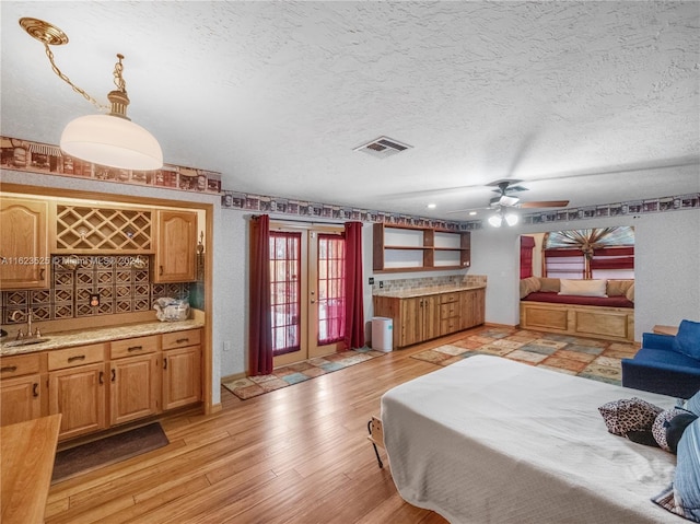 bedroom featuring french doors, bar area, a textured ceiling, and light wood-type flooring