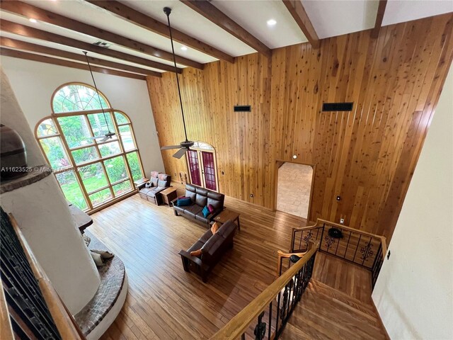 living room featuring hardwood / wood-style flooring, beamed ceiling, wood walls, and ceiling fan