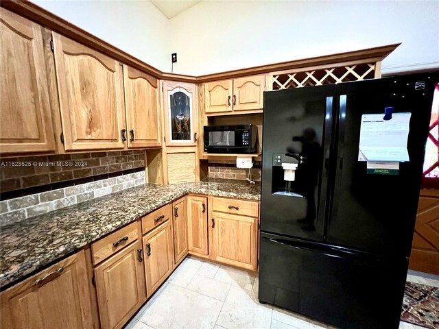 kitchen with dark stone countertops, black appliances, light tile patterned floors, and backsplash