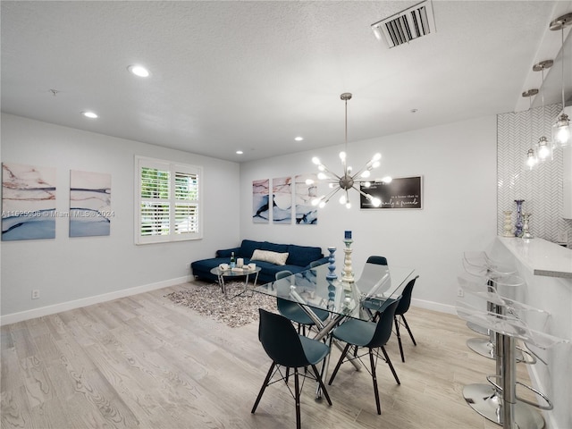 dining area featuring a textured ceiling, light hardwood / wood-style flooring, and an inviting chandelier