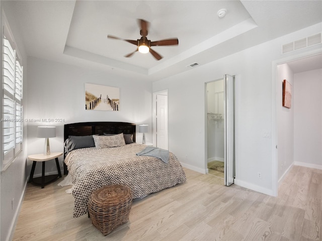 bedroom featuring ceiling fan, light hardwood / wood-style floors, and a tray ceiling